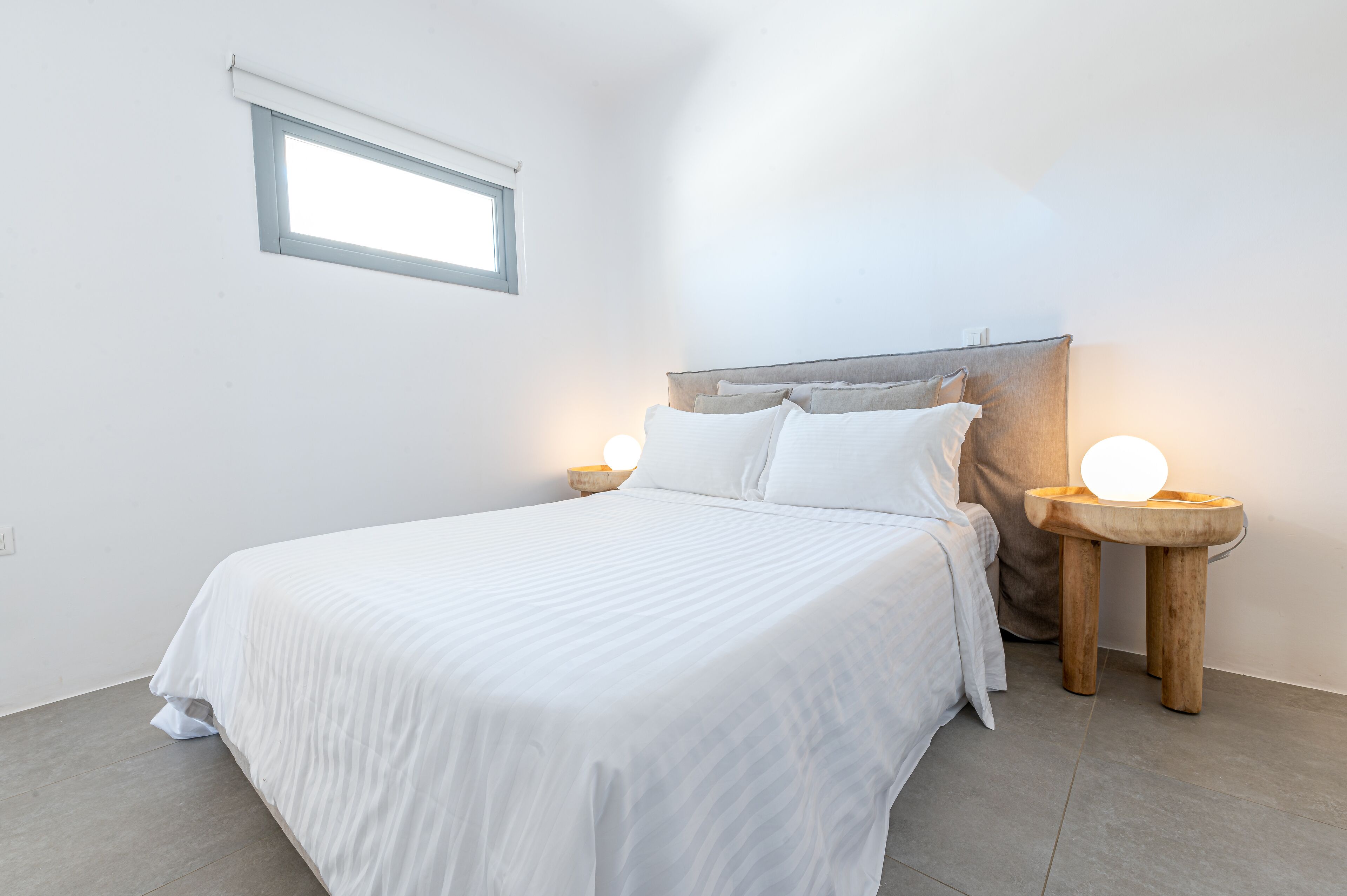 A neatly made bed with a headboard, two bedside tables with lamps, and a window above the bed.