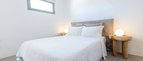 A neatly made bed with a headboard, two bedside tables with lamps, and a window above the bed.