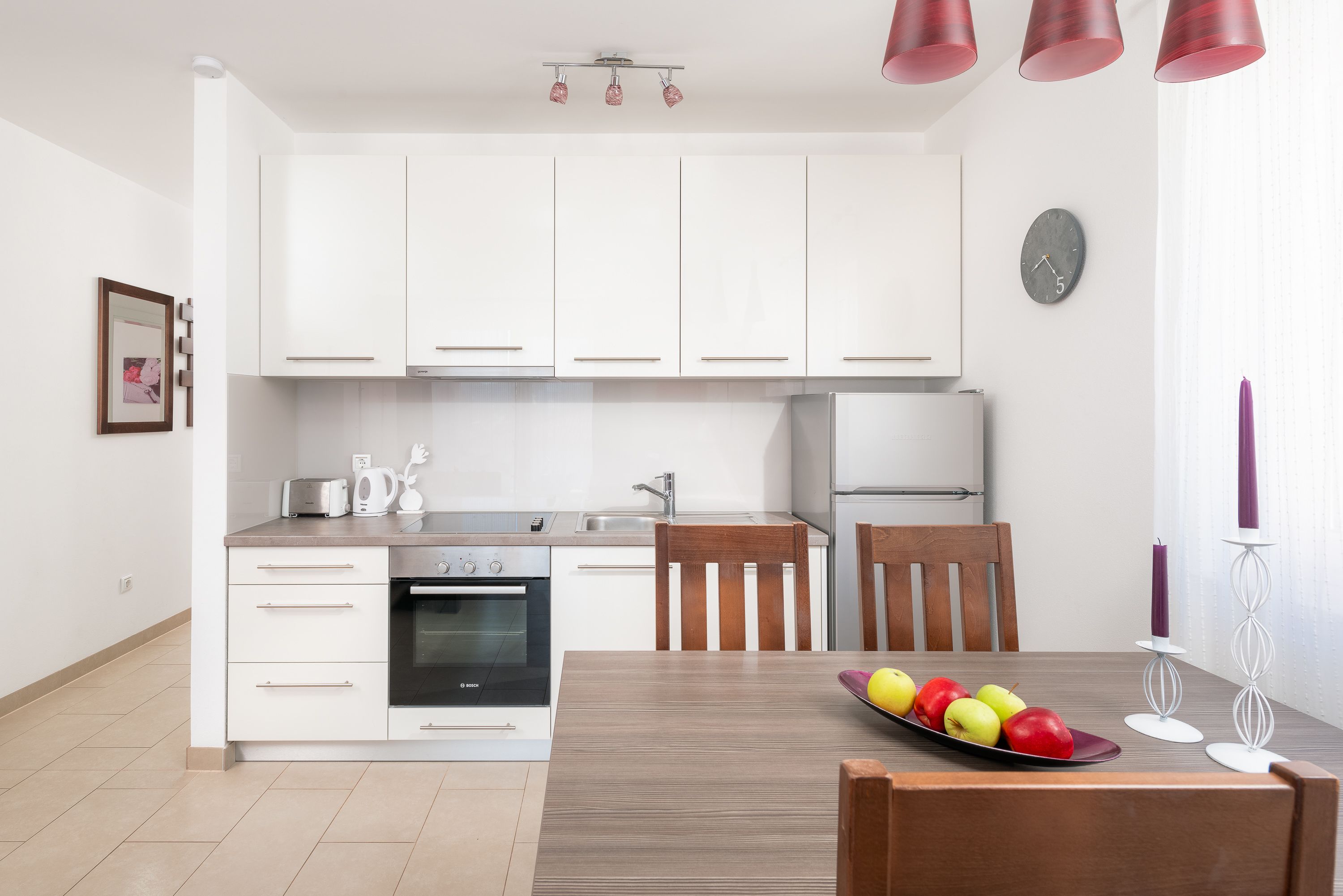 A modern kitchen with white cabinets, a dining table with chairs, and a fruit bowl.