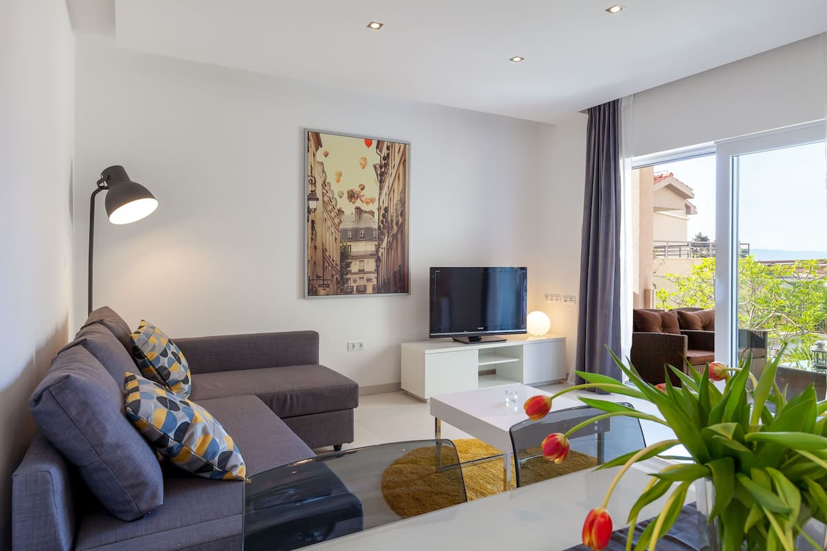 Ett modernt vardagsrum med en soffa, ett soffbord, en tv och ett stort fönster med utsikt över grönområden.