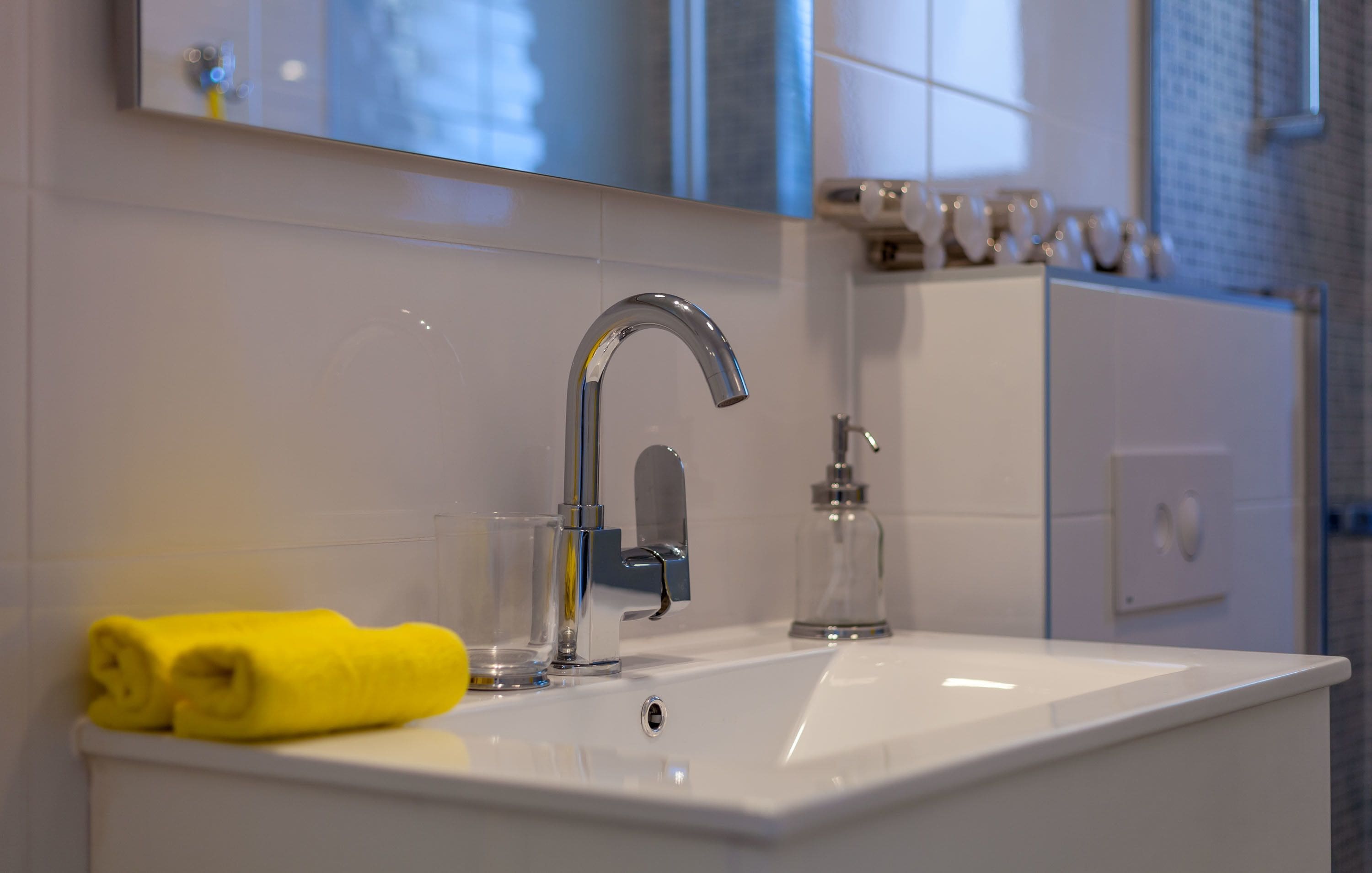 A bathroom with a white sink, a chrome faucet, a glass soap dispenser, and a yellow towel on the counter.