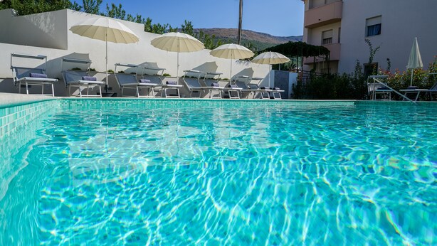 A clear swimming pool with lounge chairs and umbrellas. - Olive Tree Apartments (Podstrana)