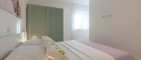 Une chambre à coucher comprenant un lit, une porte-fenêtre coulissante, une fenêtre avec des rideaux légers et un luminaire fixé au mur.