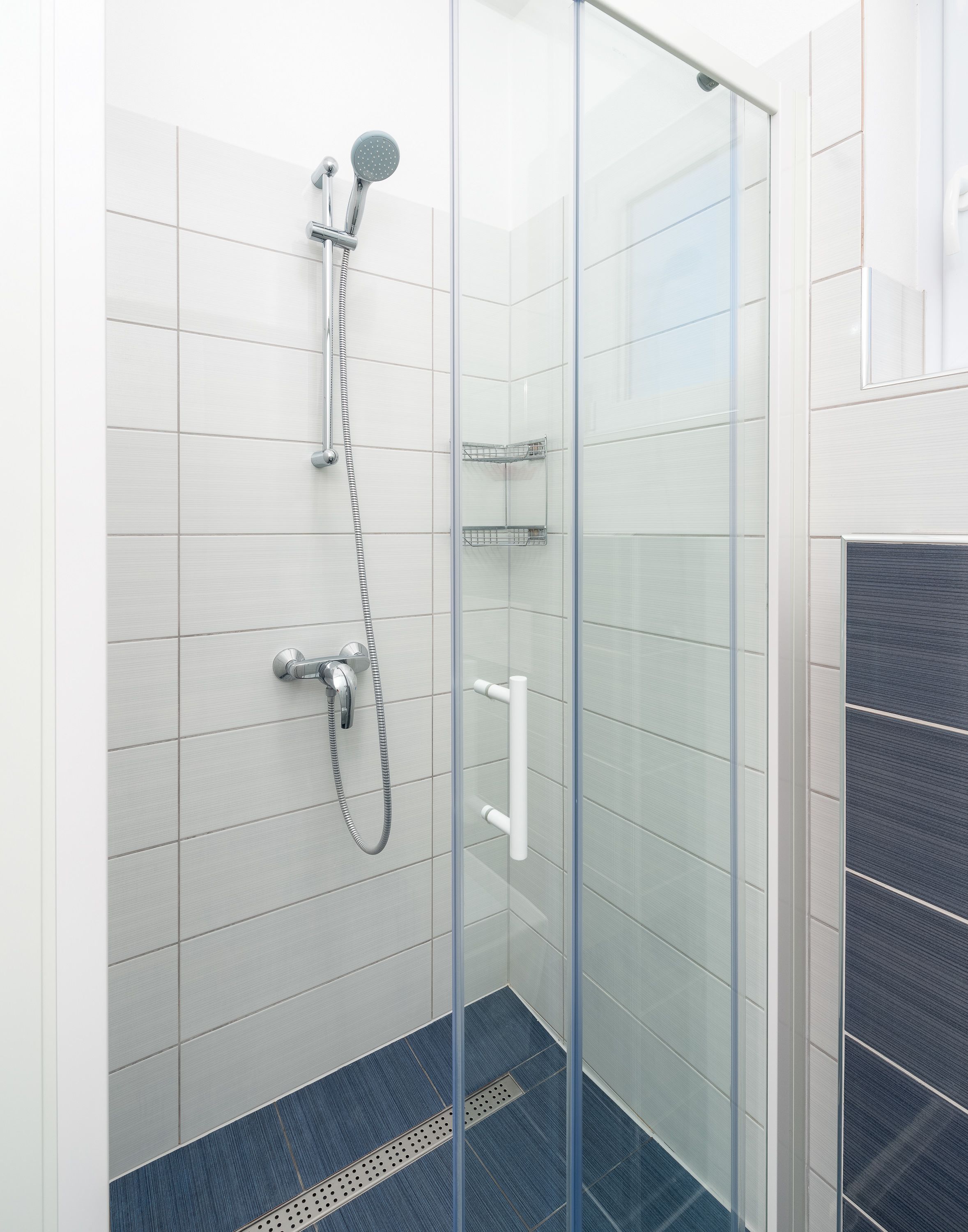 A glass-enclosed shower with a handheld showerhead and a wall-mounted faucet.