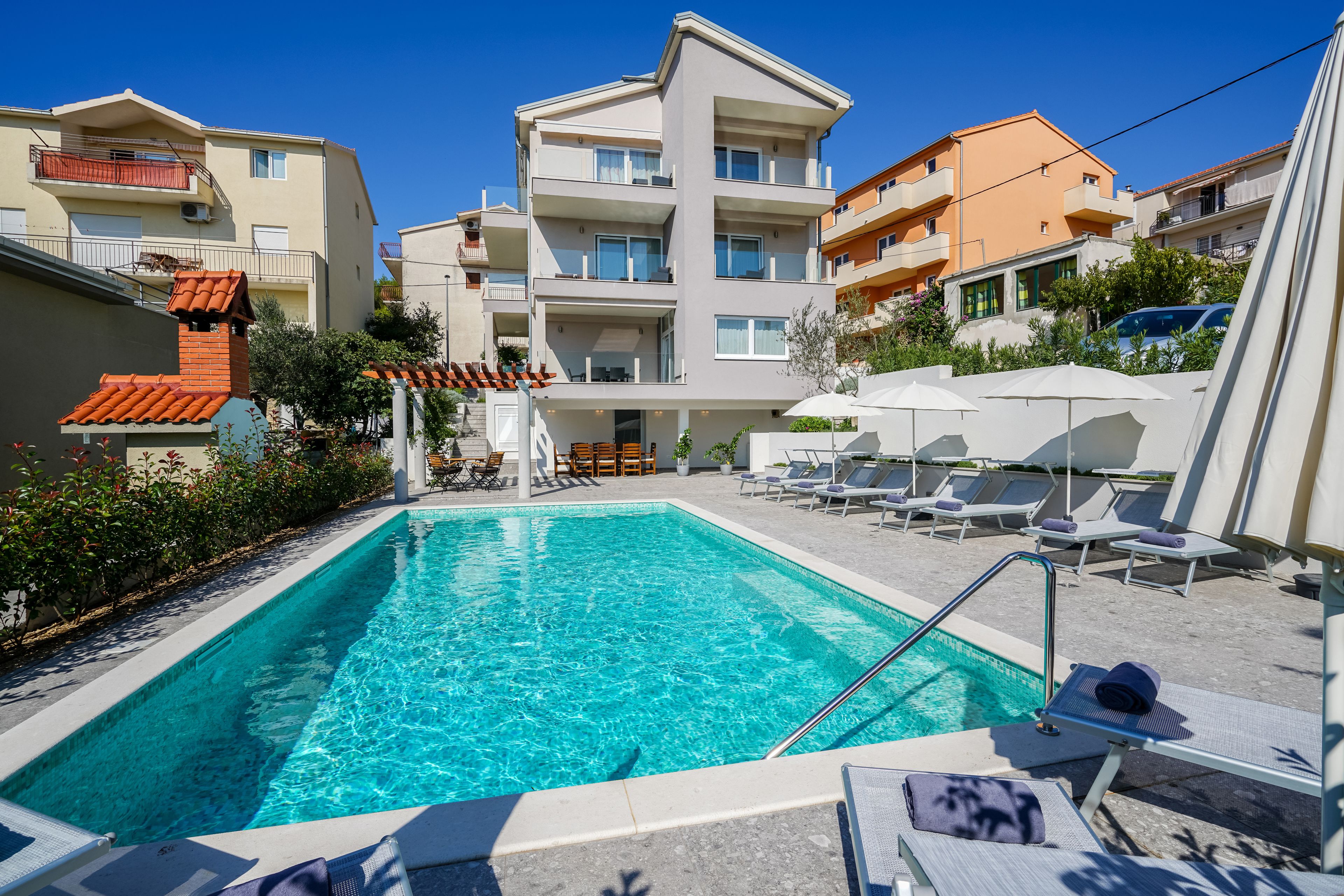 A swimming pool with lounge chairs and umbrellas, surrounded by multi-story buildings.