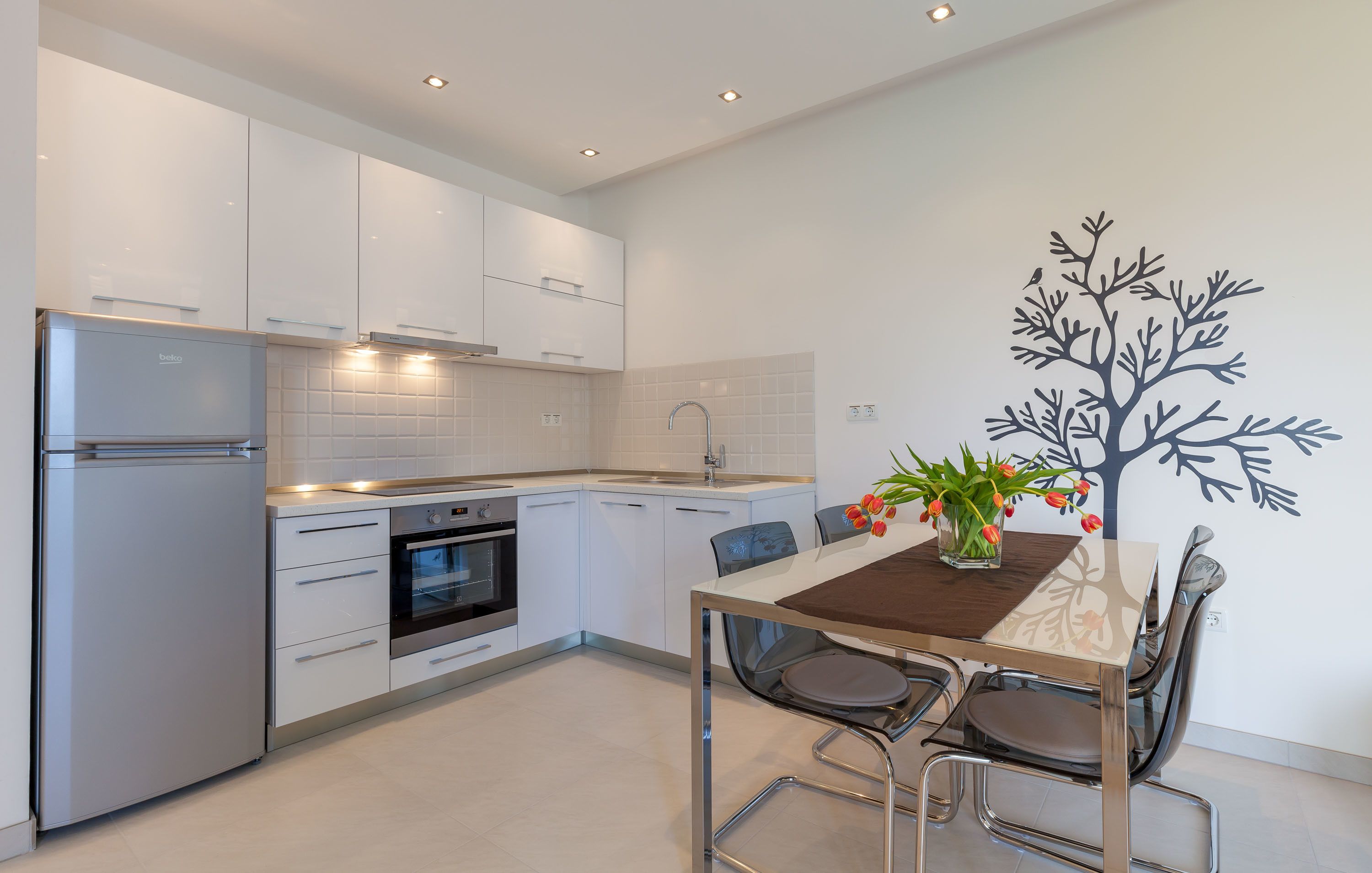 Una cocina moderna con armarios blancos, horno empotrado y zona de comedor con mesa y sillas.