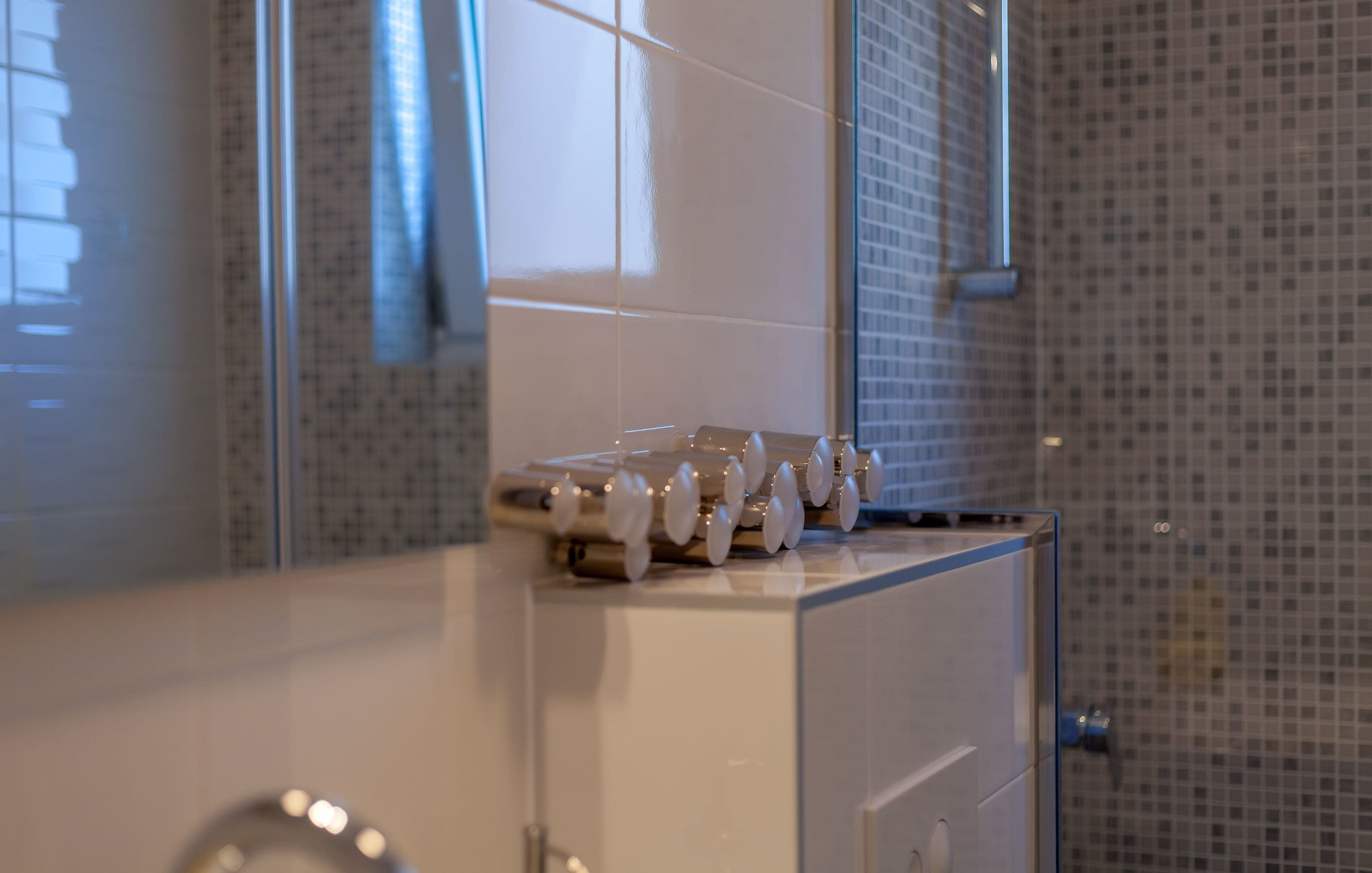 Un baño con pared de azulejos, un espejo y un lavamanos con dispensador de jabón.