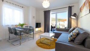 A modern living room with a sofa, coffee table, and dining area. - Olive Tree Apartments (Podstrana)