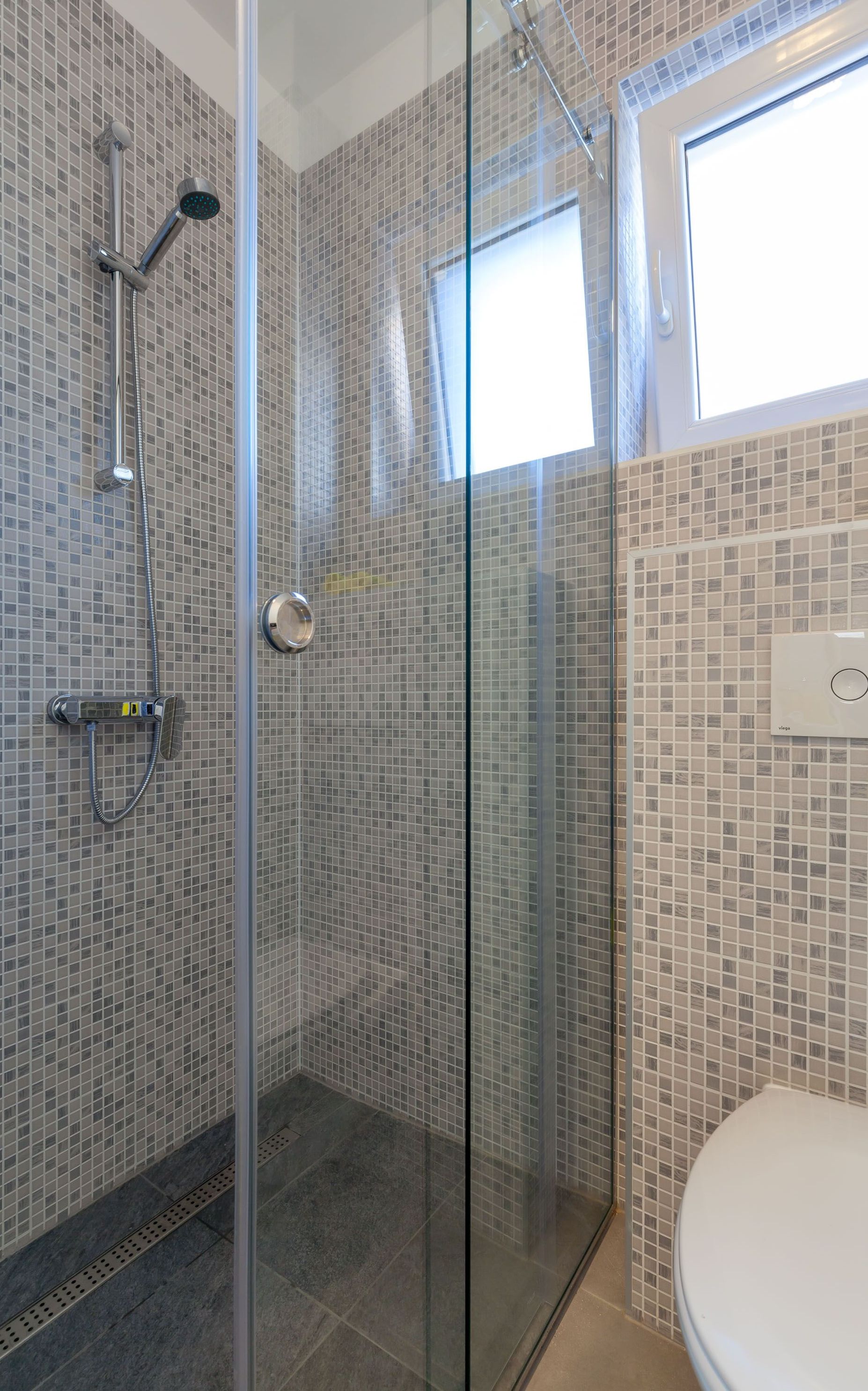 Un baño moderno con cabina de ducha de vidrio, paredes con azulejos y un inodoro.