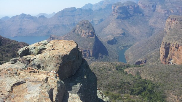 A mountainous landscape with a prominent rocky outcrop in the foreground and a valley with a body of water in the background.