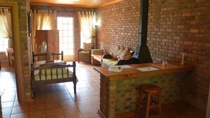 A rustic kitchen with a brick wall, wooden counter, and a chimney. There is a wooden bench and a chair in the room.