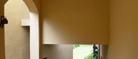 A hallway with a tiled floor, a hanging light fixture, and a view of a garden through an archway.