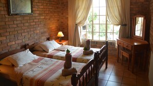 A room with two beds, a wooden dresser, a mirror, and a window with curtains.