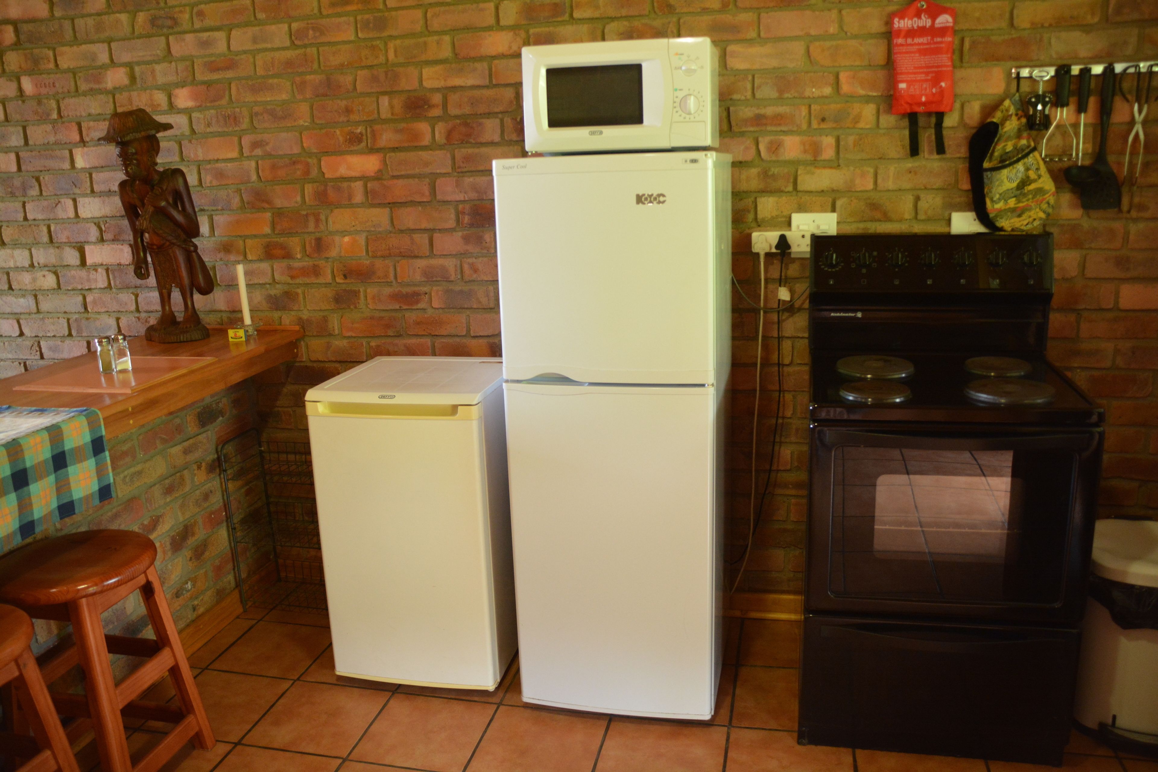 A kitchen with a refrigerator, stove, and microwave. There is a brick wall and a wooden stool.