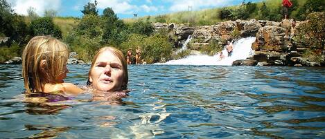 A natural hot spring with clear water, surrounded by greenery and a small waterfall.