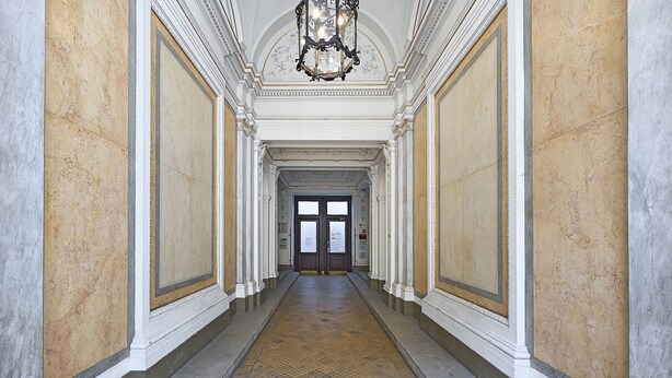 En hall med väggar klädda i marmor, ett klinkergolv och en dubbeldörr längst ner.