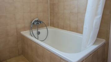 A bathroom with a bathtub, a shower hose, and a white shower curtain.
