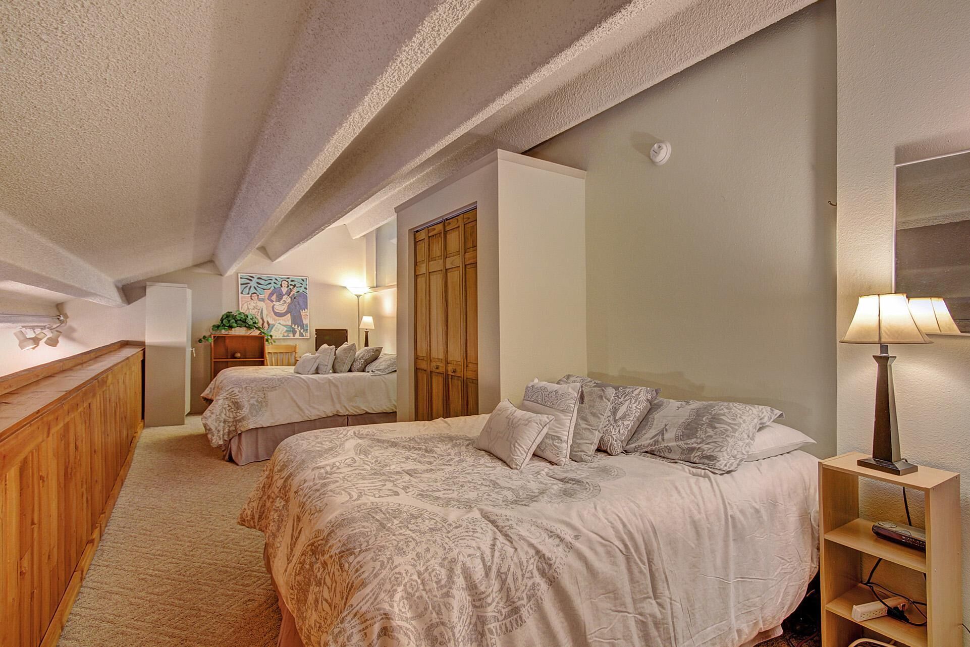 A hotel room with two beds, a wooden dresser, a desk with a lamp, and a wardrobe.