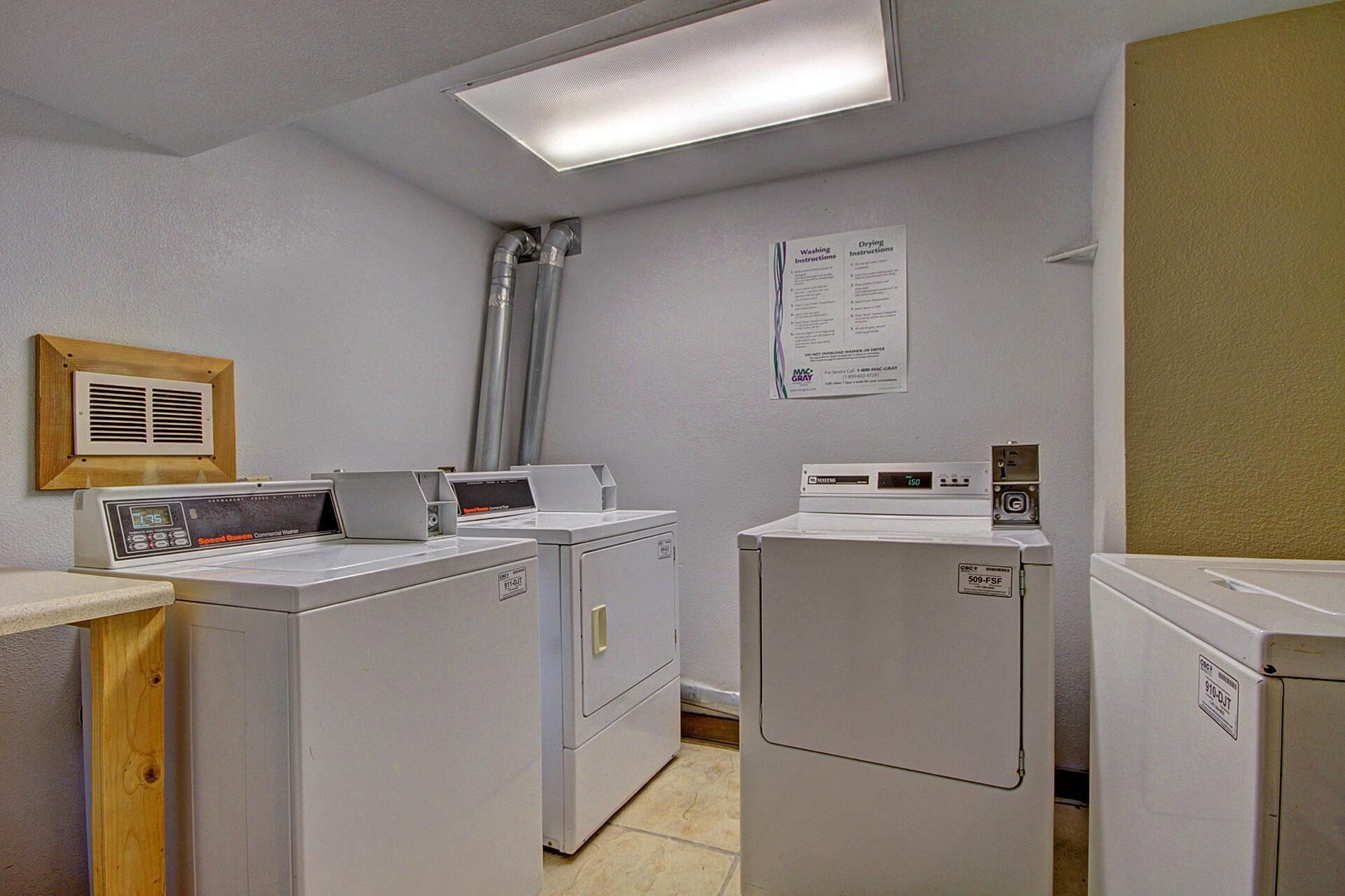 A laundry room with stacked washers and dryers, a vent, and a wall-mounted instruction sign.