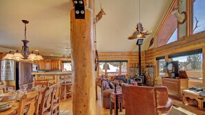A rustic cabin interior with wooden furniture, a stone fireplace, and large windows offering views of the outdoors. - Barton  4 Bedroom Home by RedAwning (Breckenridge)