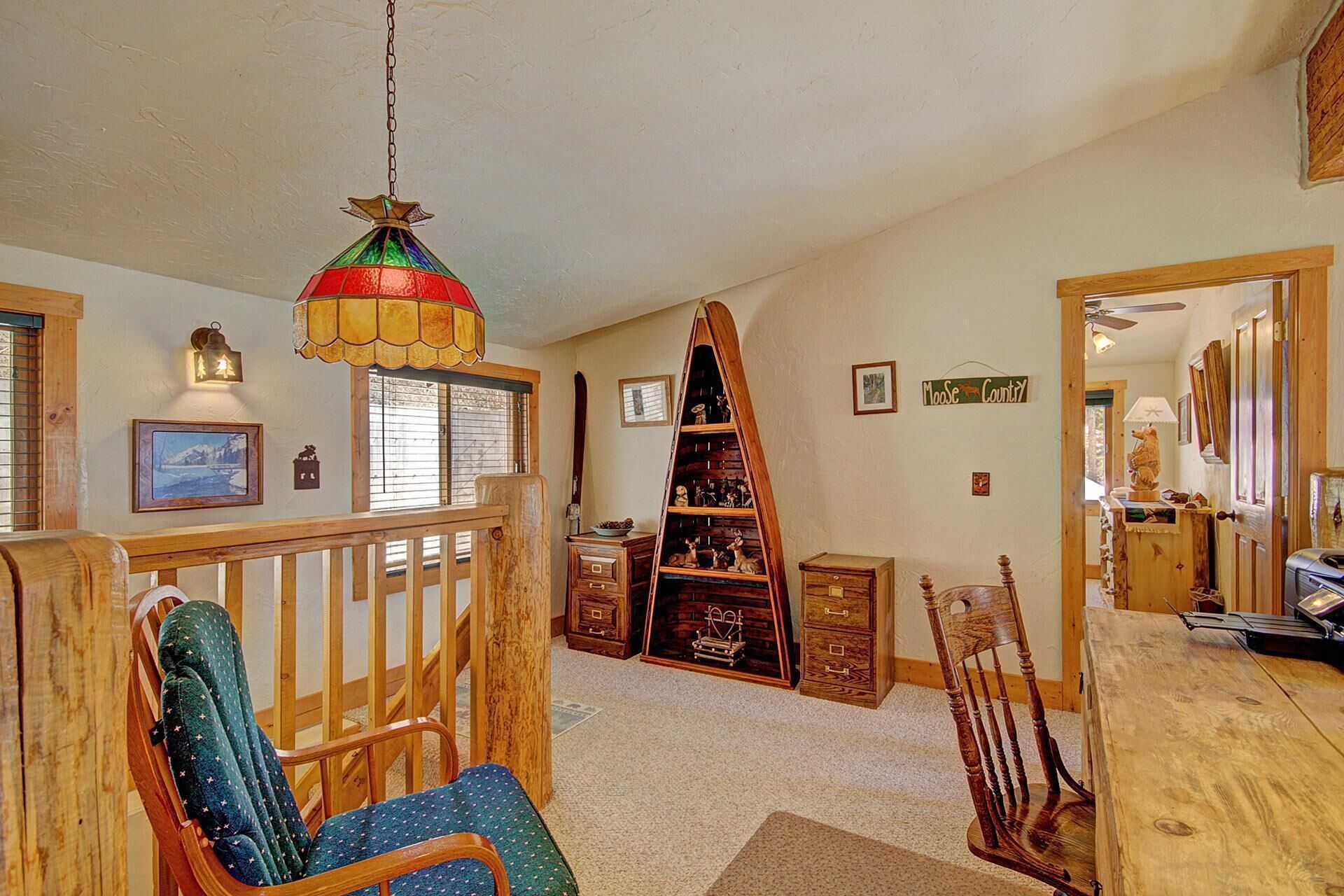 Un interior acogedor con una escalera de madera, un comedor con mesa y sillas de madera, y una estantería decorativa de madera con diversos objetos.