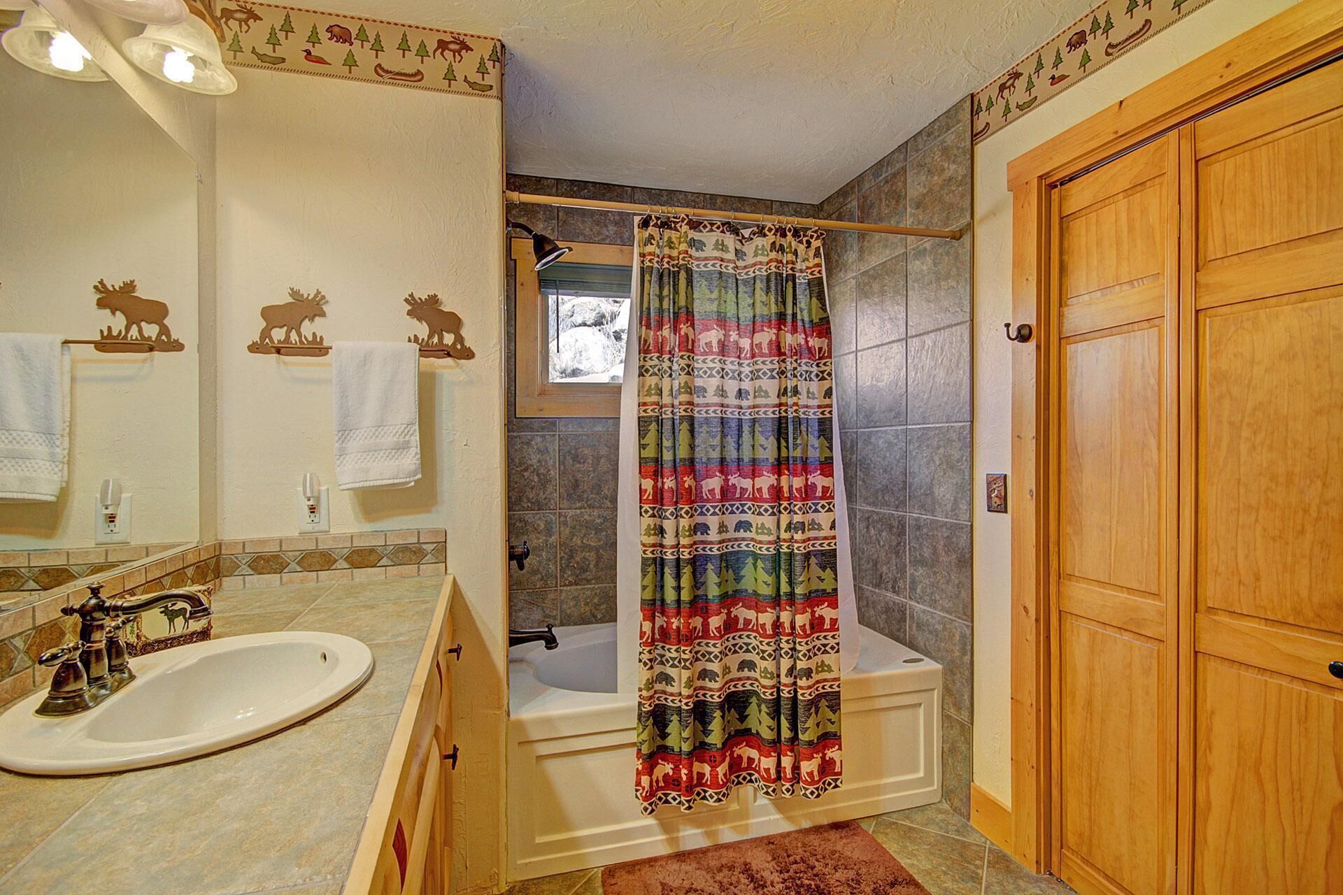 Un baño con puerta de madera, lavamanos con grifo antiguo y cortina de ducha con estampado de bosque.