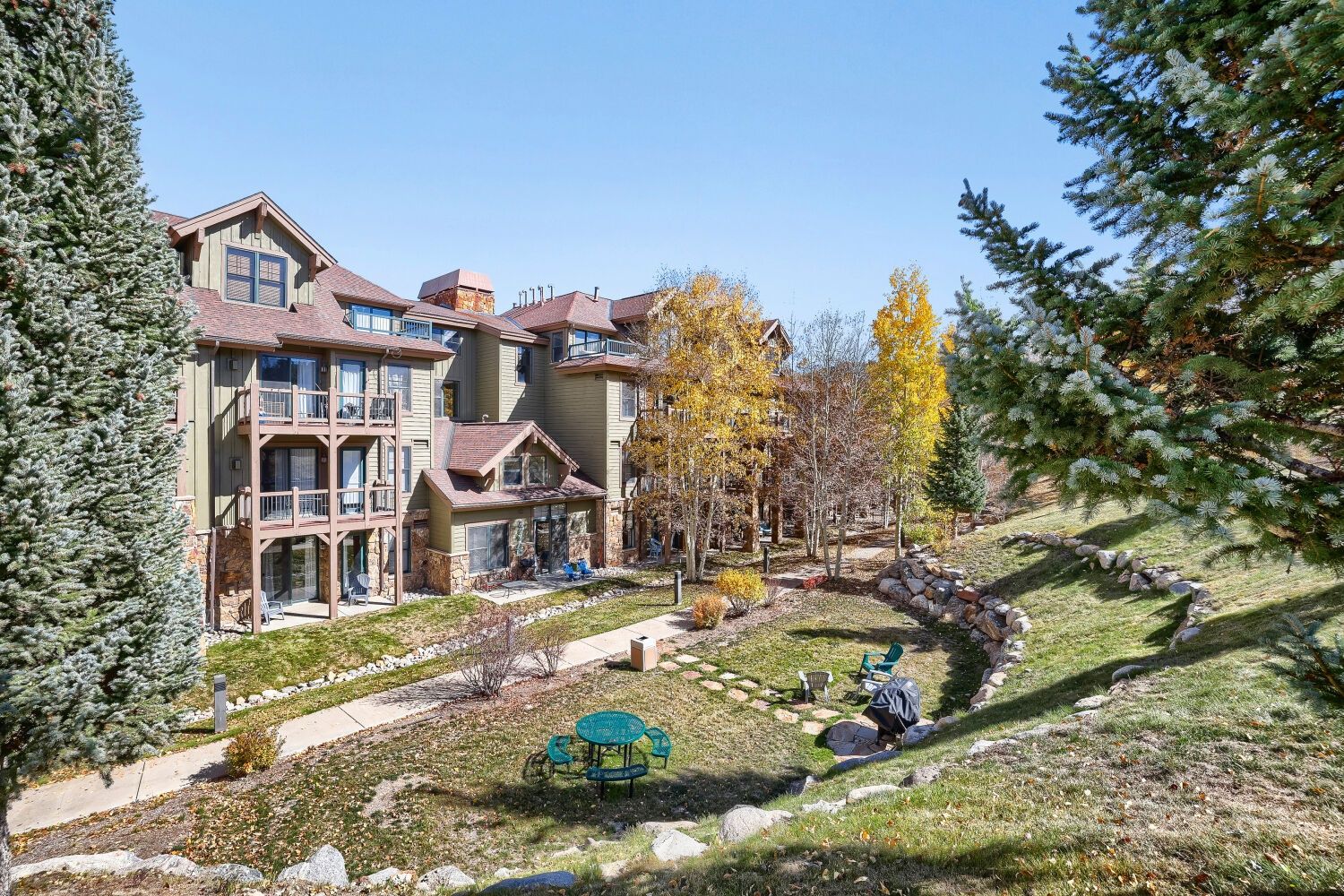 A multi-story residential building with a landscaped garden, outdoor seating, and a stone pathway.