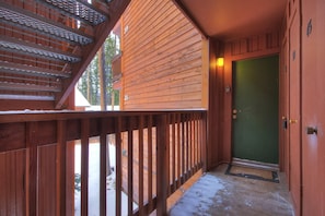 Una cabaña de madera con balcón, una puerta verde y una escalera.