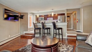 A modern kitchen with a central island, bar stools, and a dining table in a living area with a sofa and a rug. - Peak 8 Ge E35 2 Bedroom Condo by RedAwning (Breckenridge)