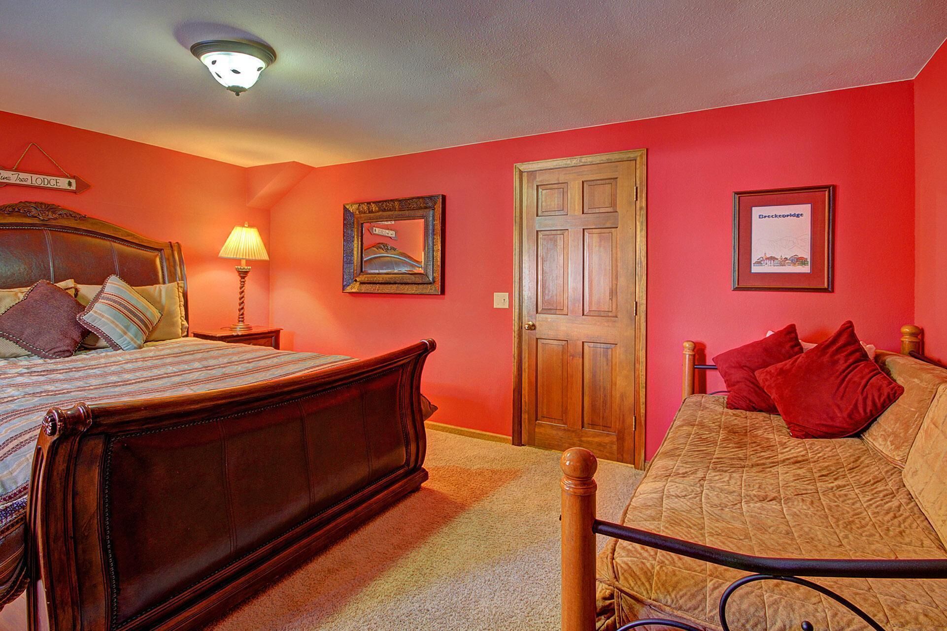 A bedroom with a wooden bed, a nightstand with a lamp, a door, and two framed pictures on the wall.