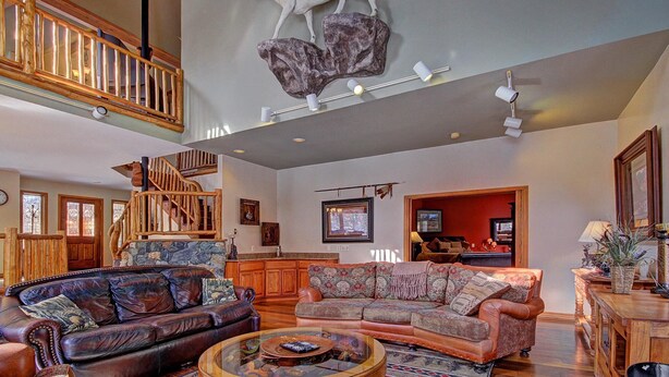 A spacious living room with a high ceiling, a wooden staircase, and a mounted animal head.
