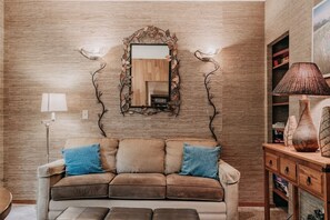 Una sala de estar con pared de madera, un sofá con cojines, un espejo y una lámpara.