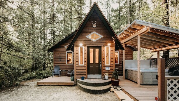 Een chalet met een veranda, buitenzitplaatsen en een jacuzzi.