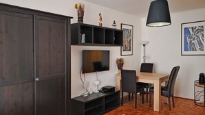 Une chambre d’hôtel moderne dotée d’une grande armoire, d’un téléviseur à écran plat, d’une table à manger avec des chaises et d’un plancher en bois.