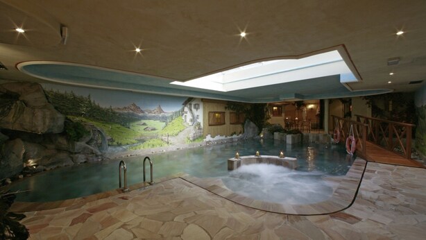 Un espace spa doté d’un bain à remous, d’un sol en pierre et d’une fresque représentant un paysage montagneux.