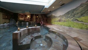 Un espace de bien-être comprenant un jacuzzi, un sol en pierre et une fresque représentant un paysage montagneux.