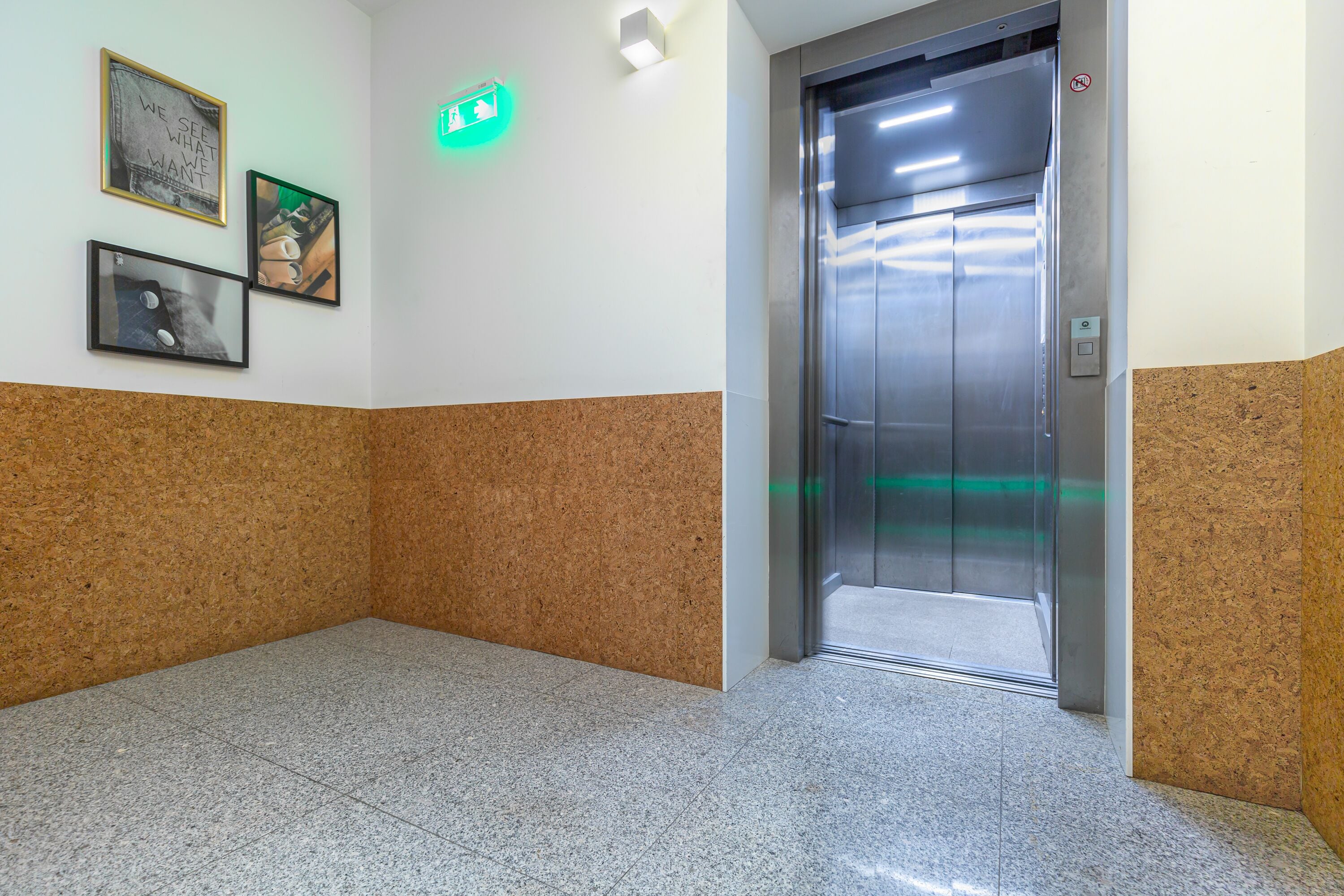 A clean, modern elevator area with a cork wall, a tiled floor, and a framed picture on the wall.
