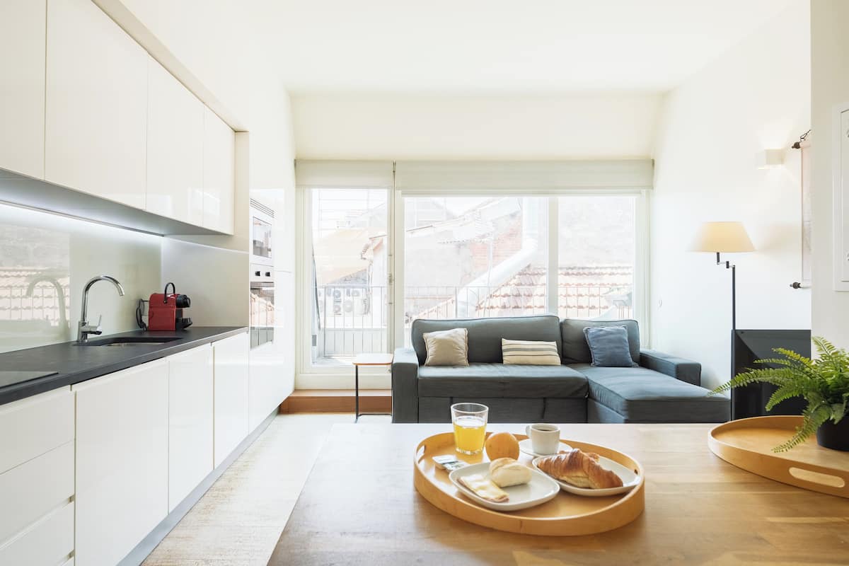 A modern kitchen with white cabinets, a grey sofa, and a dining area with a tray of food and drinks.