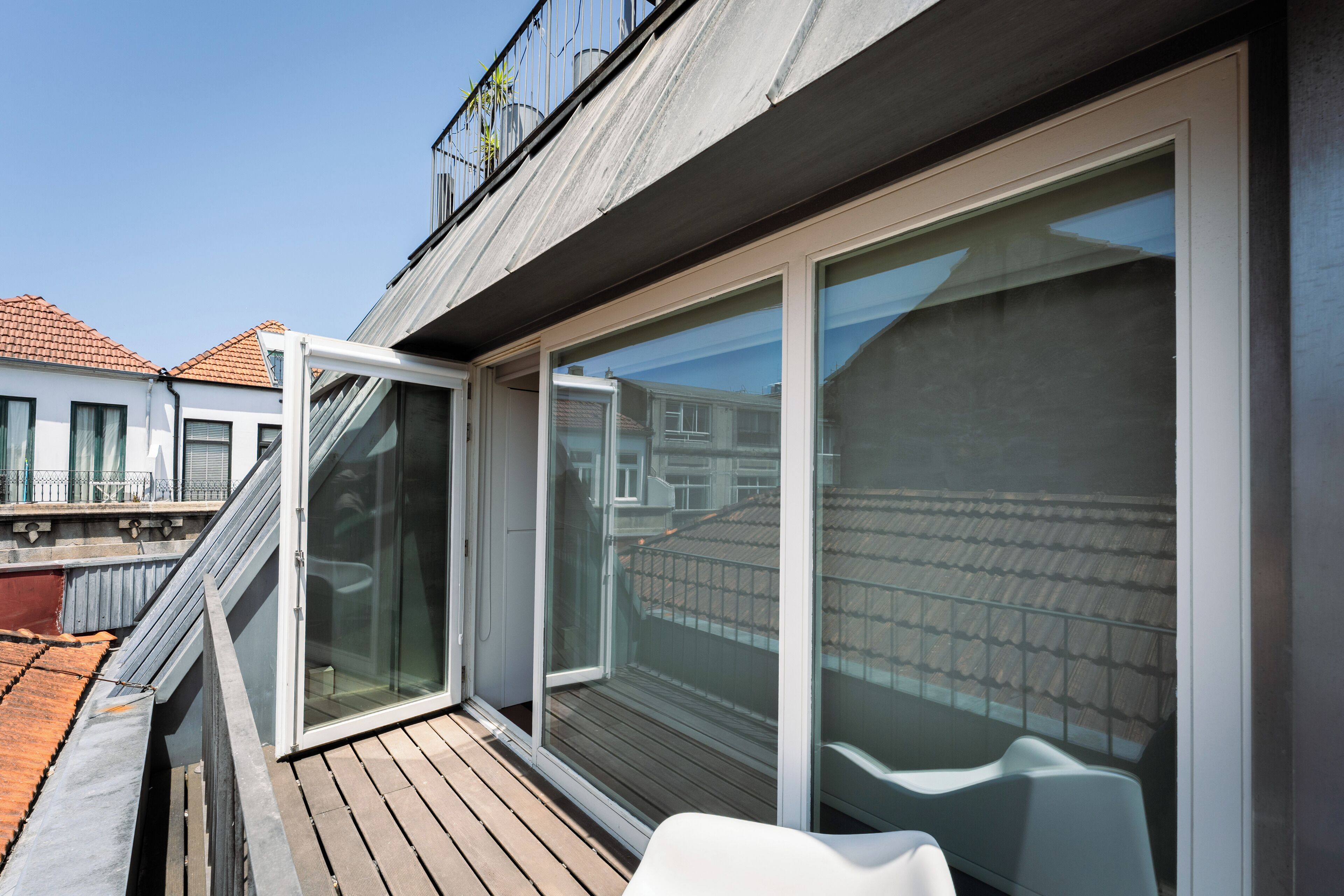 A modern balcony with a wooden floor, a glass door, and a white chair.
