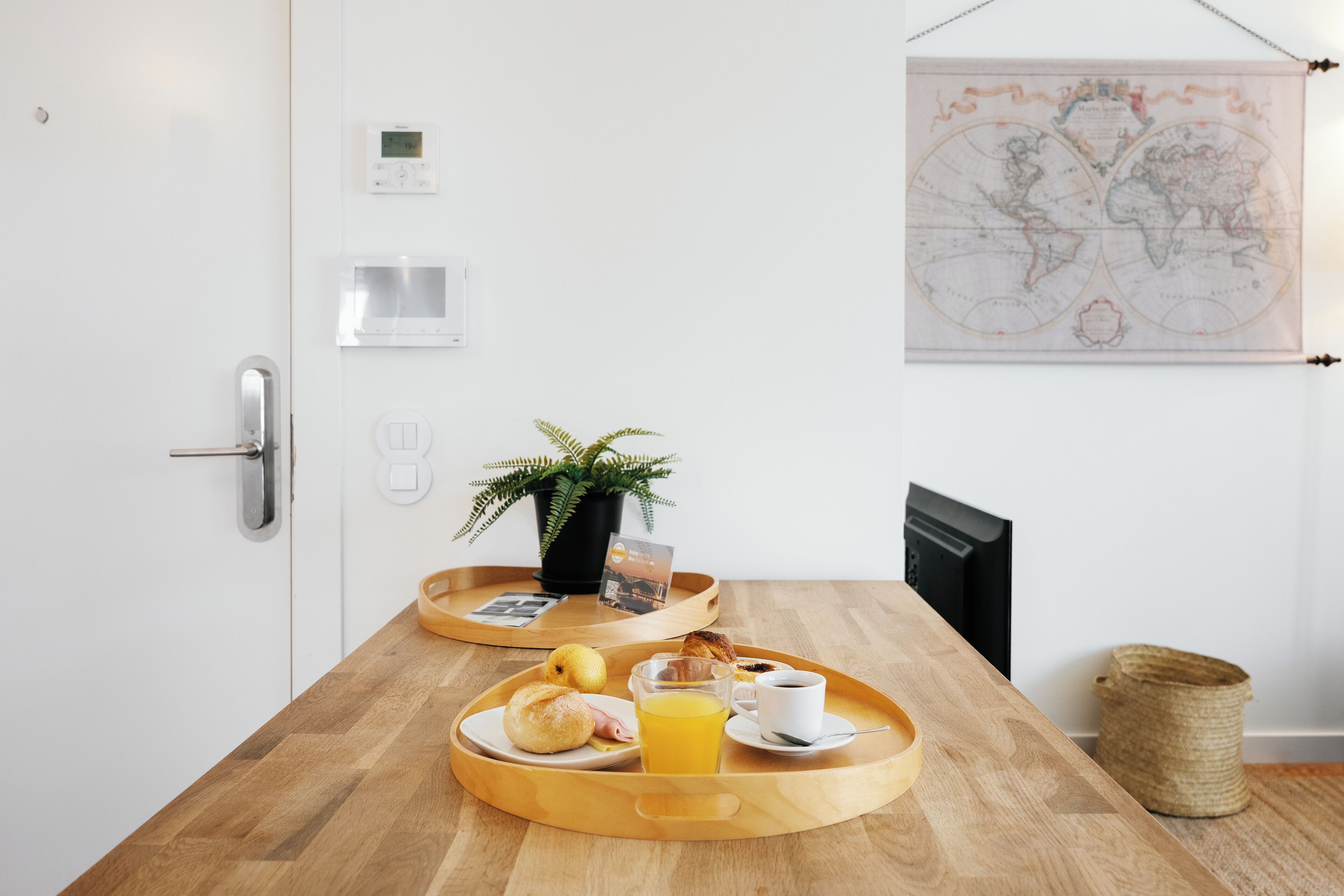A breakfast tray with croissants, a glass of orange juice, and a cup of coffee on a wooden table in a room with a world map on the wall.