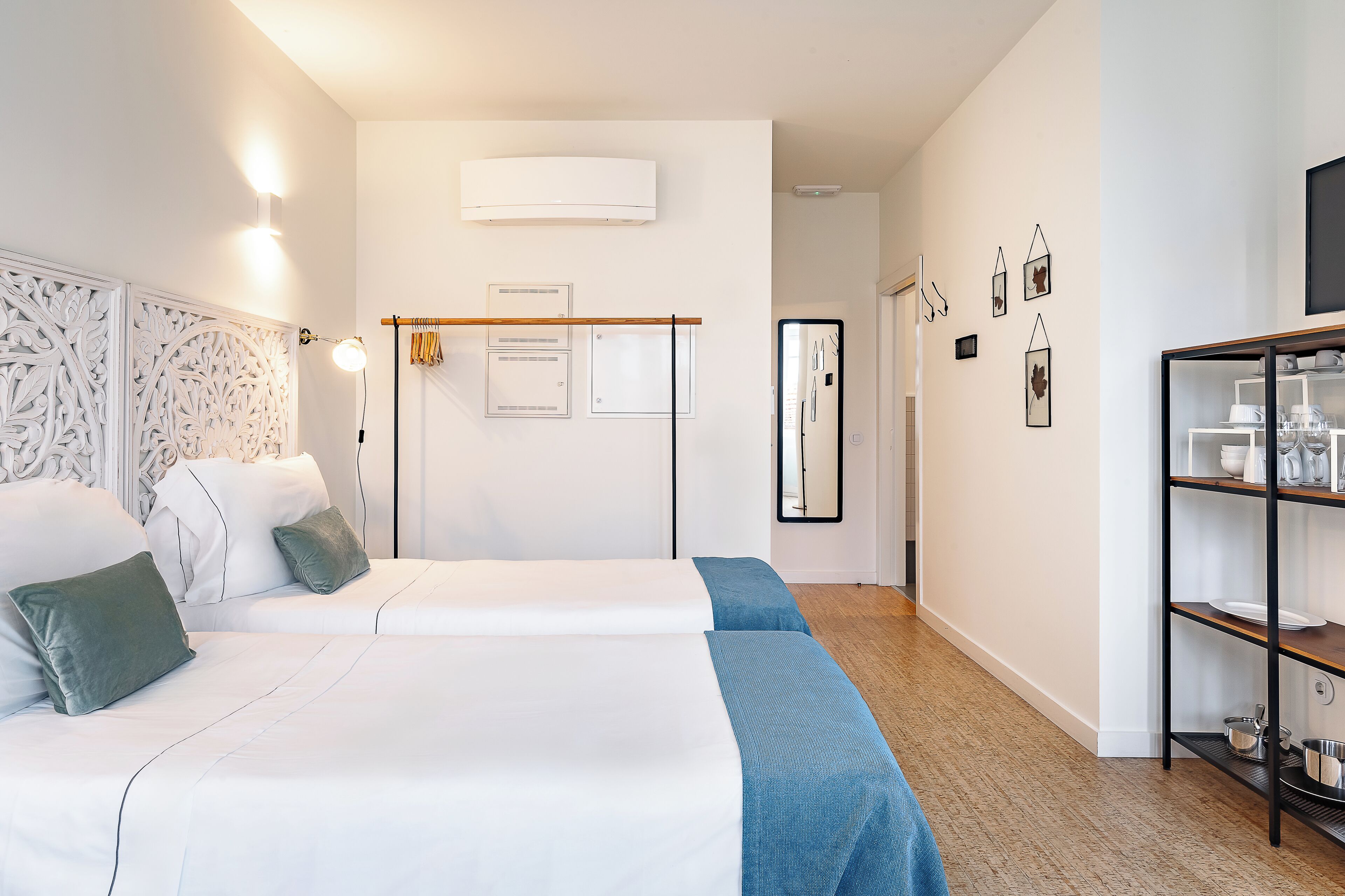 Et hotelværelse med to senge, et klædeskab, en hylde med toiletartikler og en fastgjort aircondition.