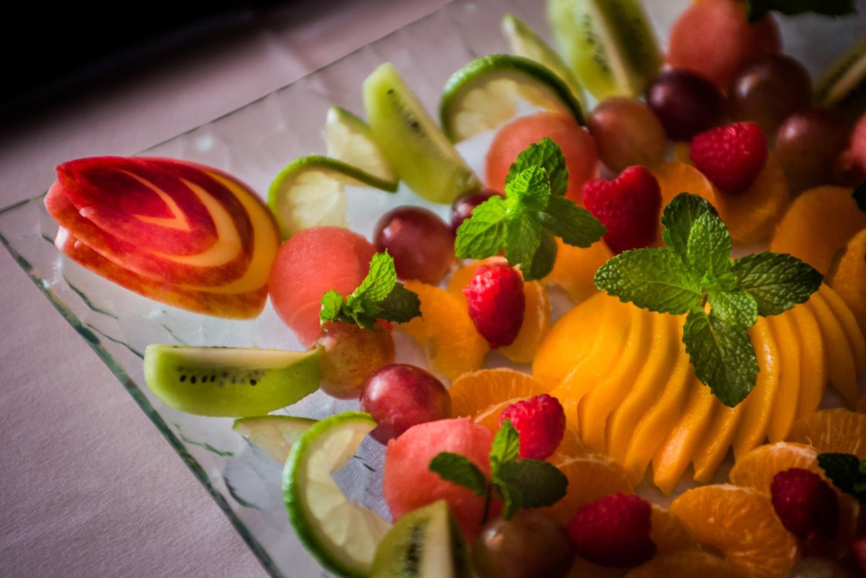 A glass plate with various sliced fruits and mint leaves.