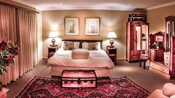 Una habitación de hotel con una cama grande, dos mesitas de noche con lámparas, un aparador, un espejo y una alfombra roja estampada.