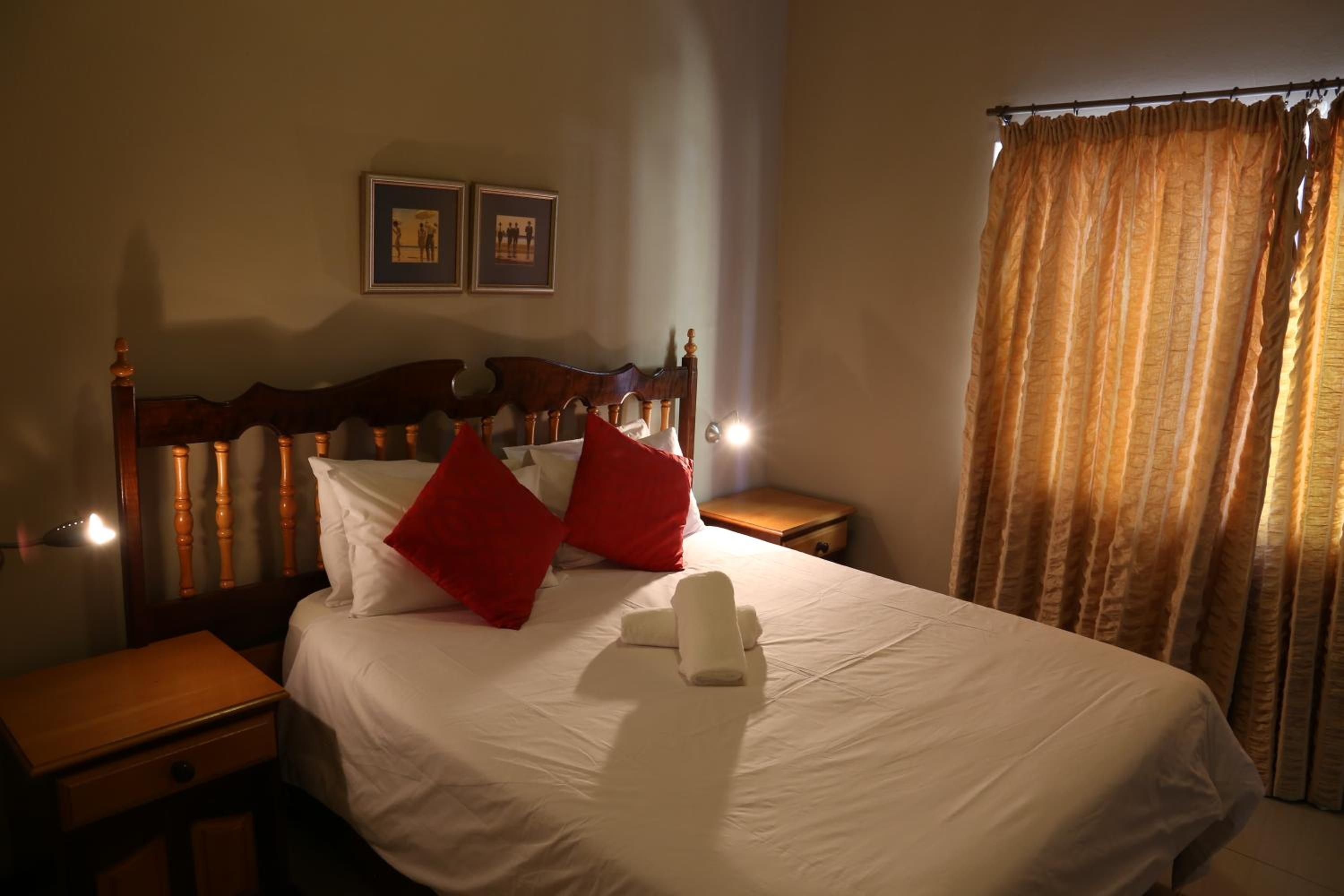 Habitación de hotel con una cama grande, dos mesitas de noche, un cabecero de madera y un ventanal con cortinas.