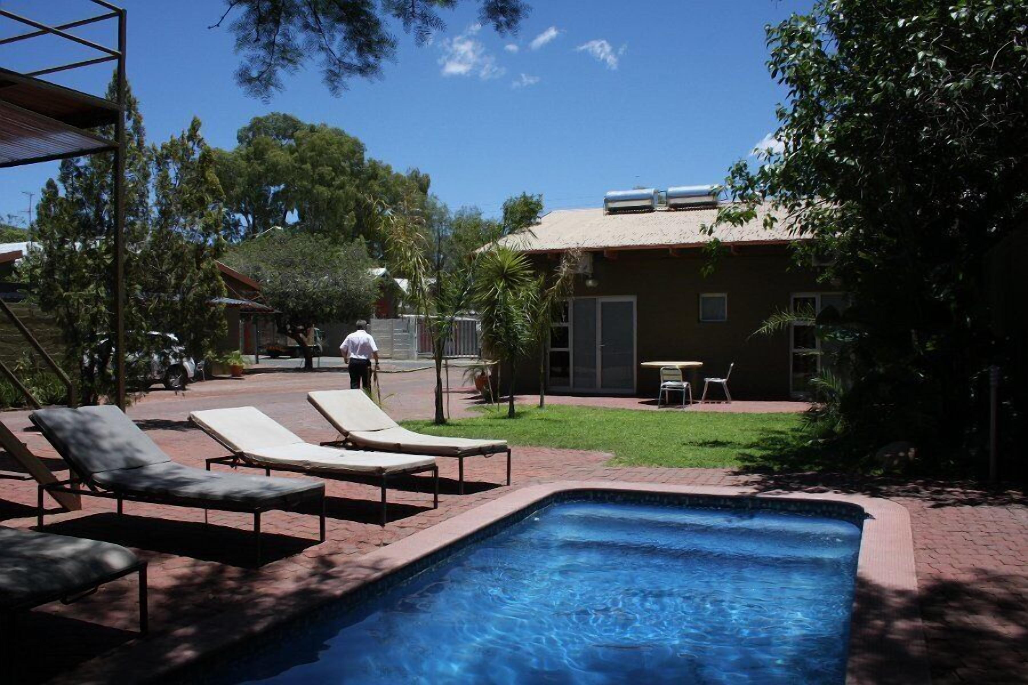 A swimming pool with lounge chairs, a grassy area, and a building with a tiled roof.