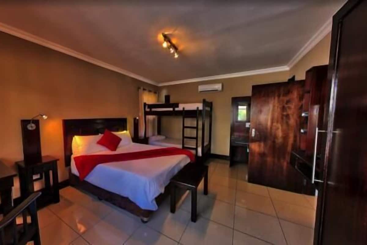Una habitación de hotel con literas, un escritorio, una silla, un armario y una lámpara de techo.