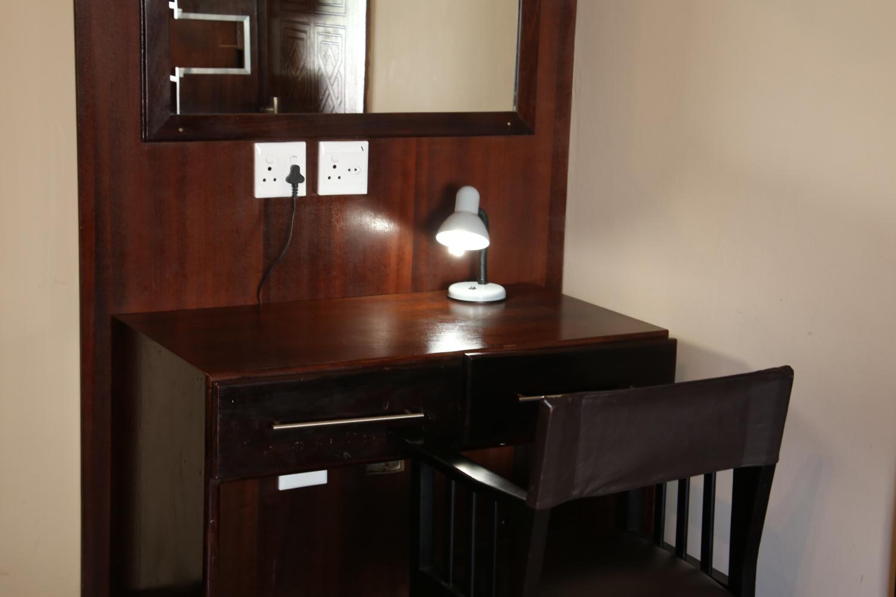 A wooden desk with a lamp, a chair, and a mirror above the desk.