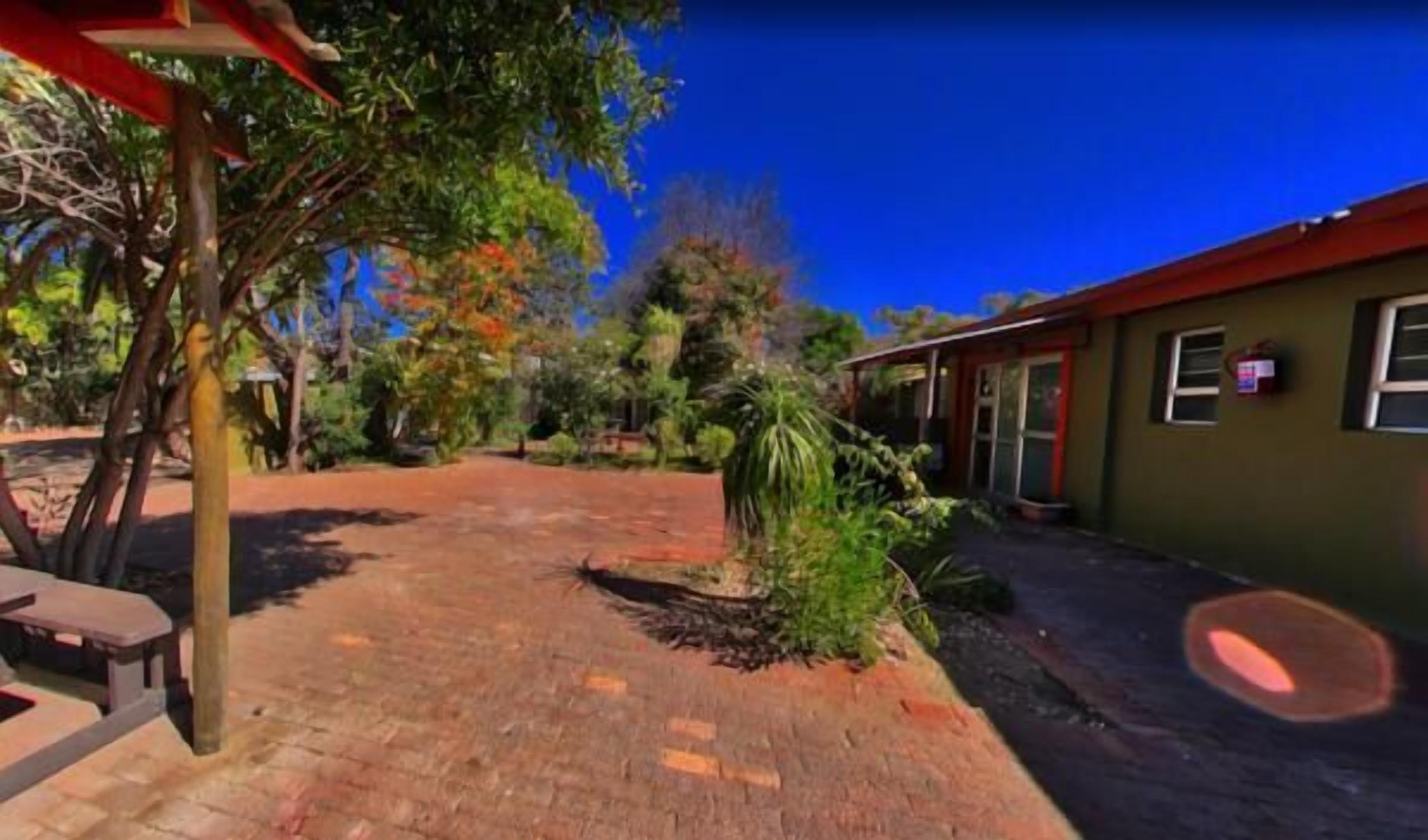 Una casa con patio de ladrillo, pequeño jardín y tejado rojo.