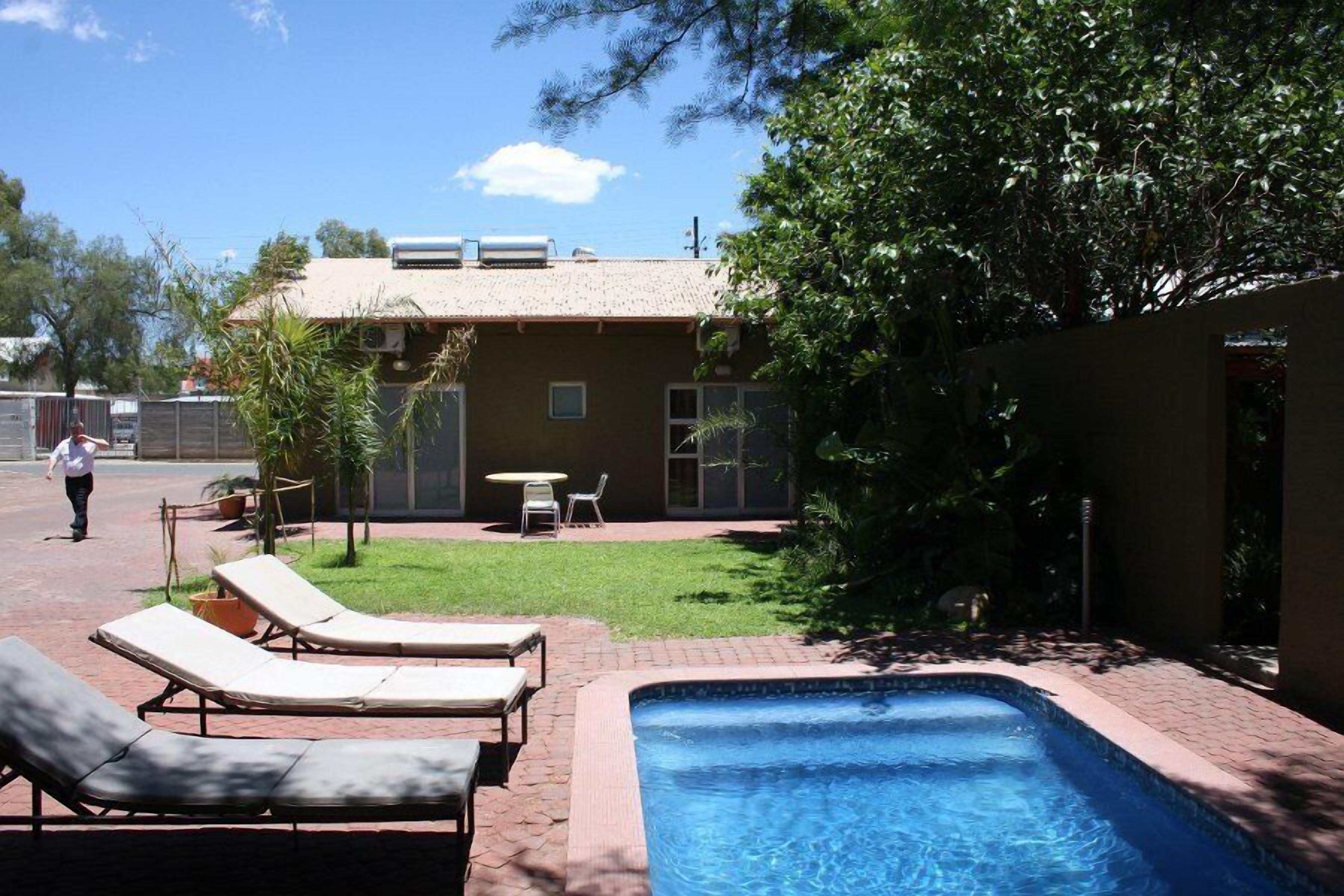A backyard with a swimming pool, lounge chairs, and a small patio area.