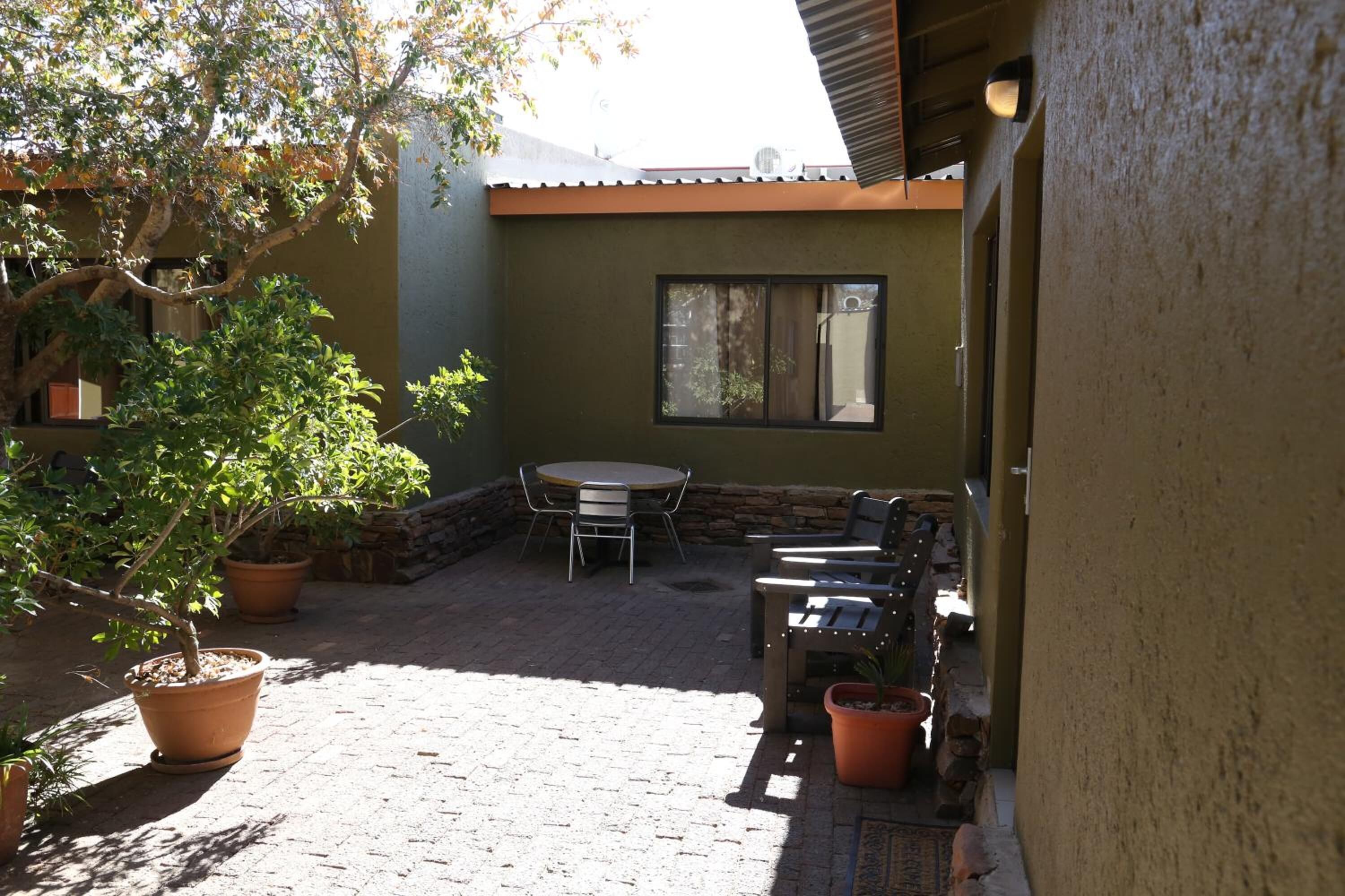 An outdoor patio area with a brick floor, a table and chairs, and potted plants.